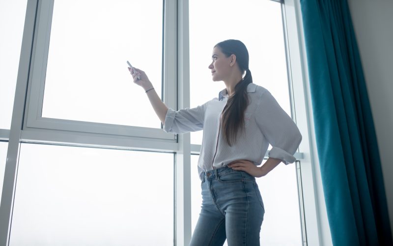 Concentrated lady using a remote control for closing the blinds